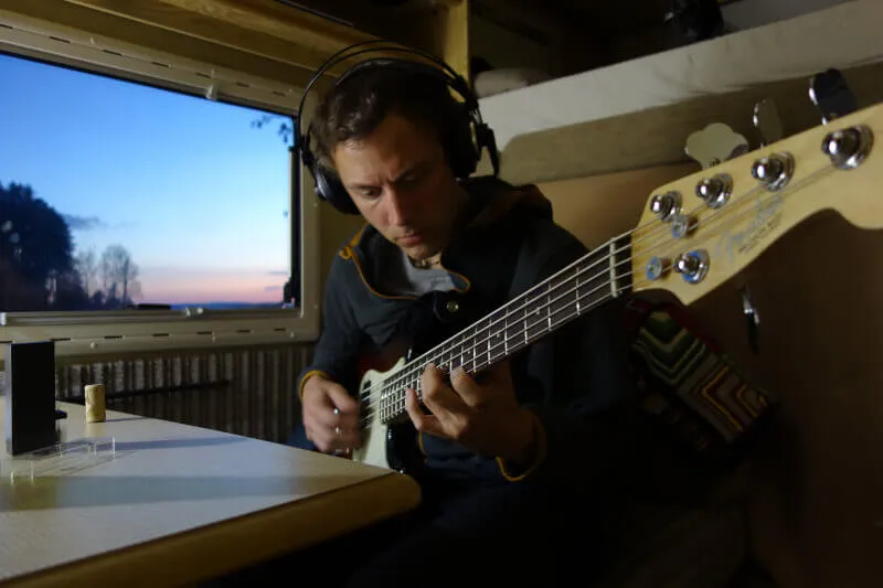 Andy spielt Bass im Camper, während draußen die Dämmerung einsetzt.